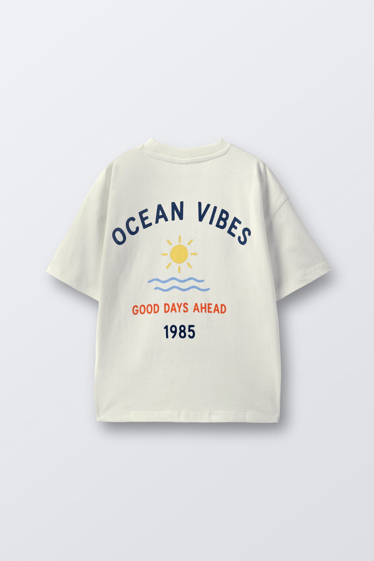 Off-white comfort tee with back “Ocean Vibes” print, sun, waves, and 1985