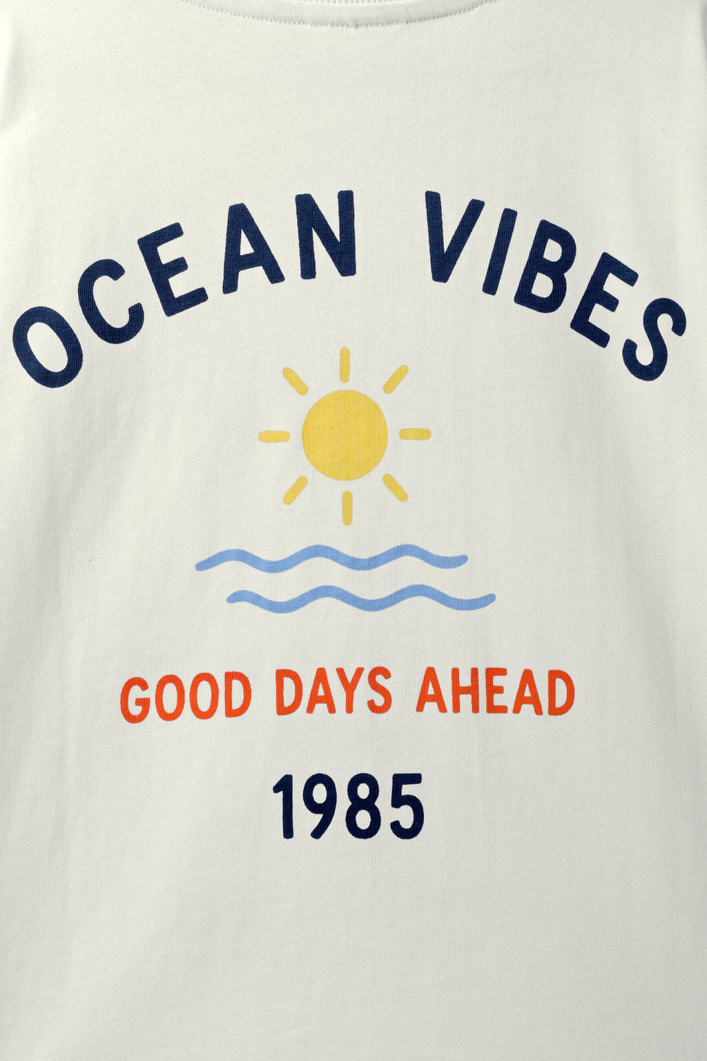 Off-white tee close-up showing “Ocean Vibes” text, sun icon, waves, and 1985