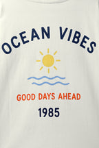 Off-white tee close-up showing “Ocean Vibes” text, sun icon, waves, and 1985
