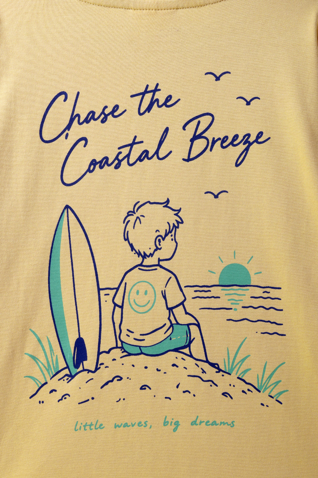 Sand yellow tee front print: 'Chase the Coastal Breeze' with surf boy illustration.
