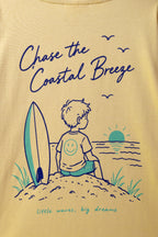 Sand yellow tee front print: 'Chase the Coastal Breeze' with surf boy illustration.
