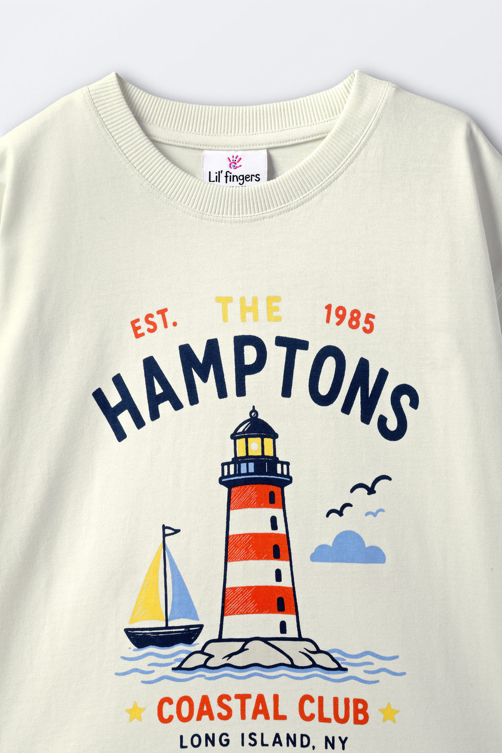 Off-white comfort tee with “The Hamptons” lighthouse graphic and Coastal Club logo