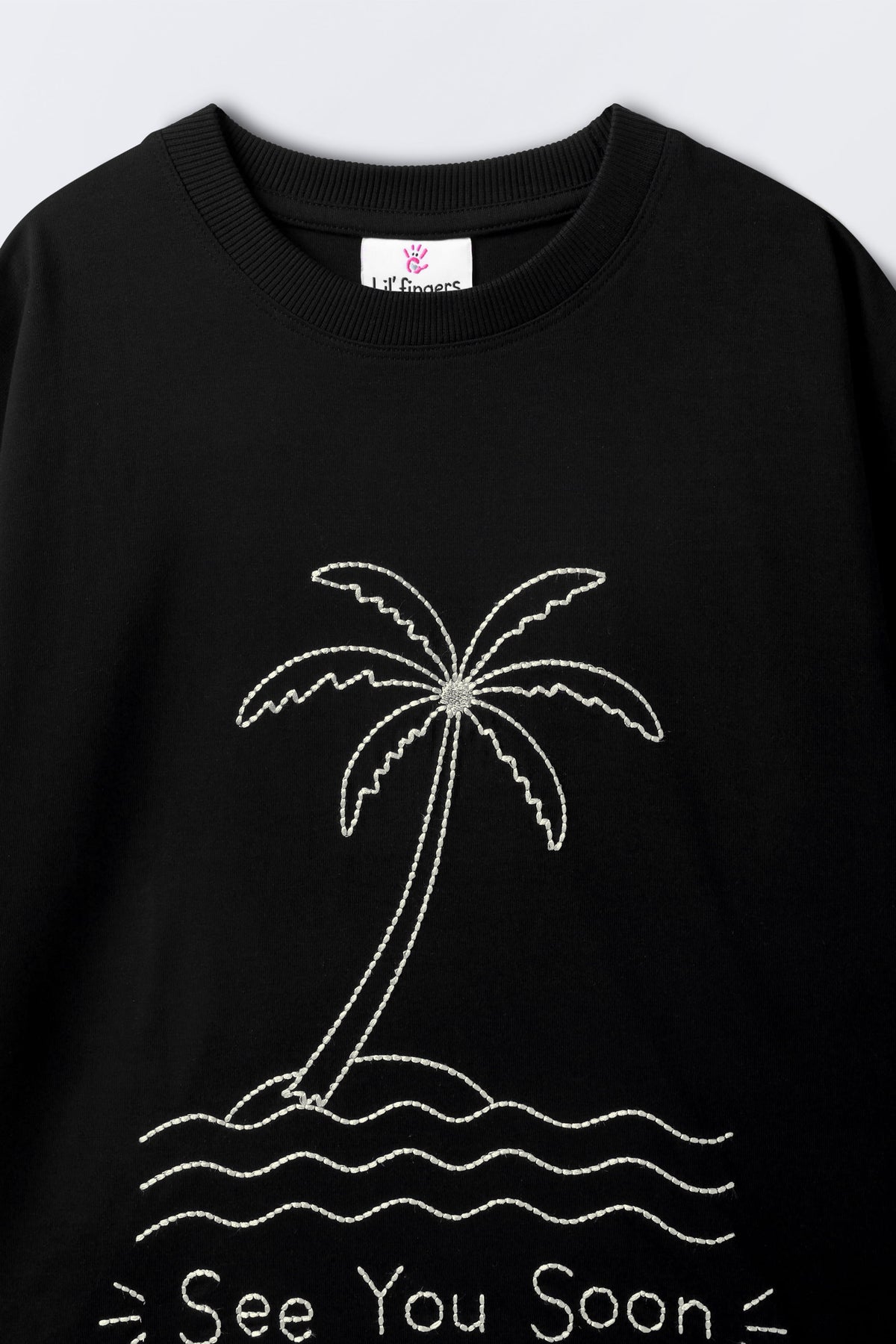 Black oversized T-shirt close-up showing crew neck and palm tree graphic