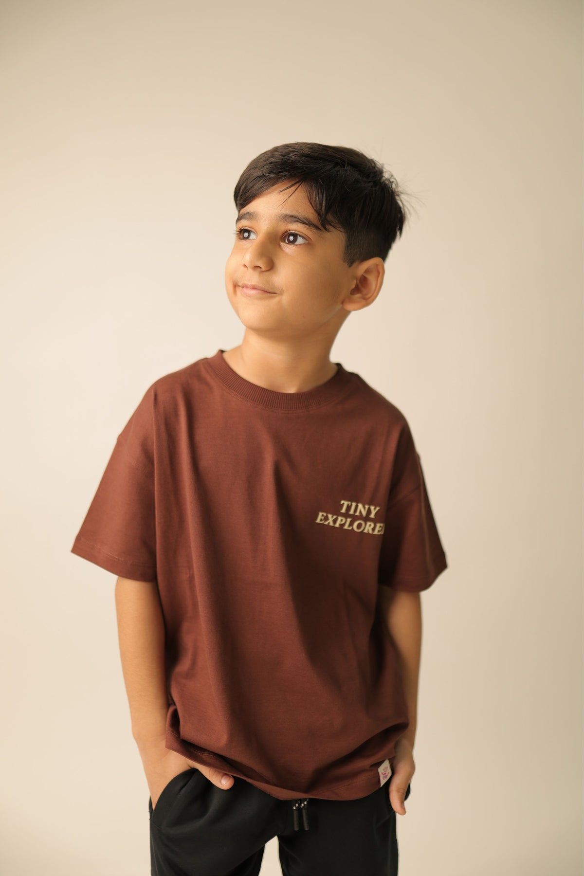 Brown kids' T-shirt on model with small front “TINY EXPLORER” print, short sleeves