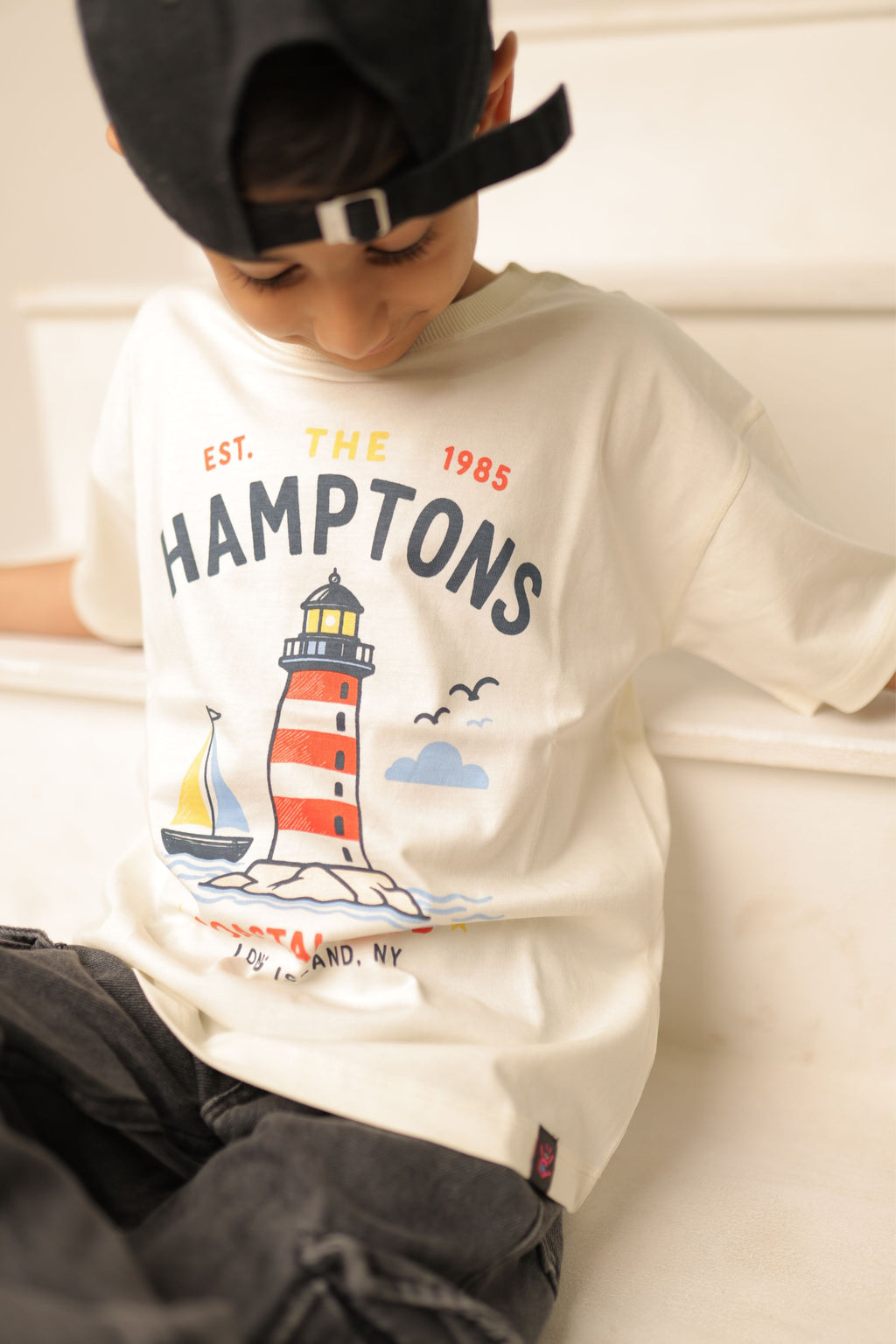 Off-white comfort tee with “The Hamptons” lighthouse graphic worn by a child