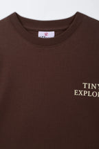 Brown crew-neck kids' T-shirt close-up of “TINY EXPLORER” front print