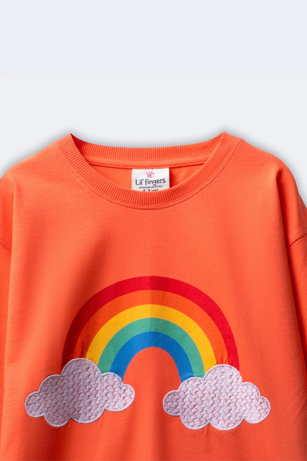 Girl’s coral T-shirt close-up: rainbow print with embroidered clouds on the front