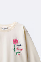 Off-white long-sleeve tee with “good things grow” pink flower graphic detail