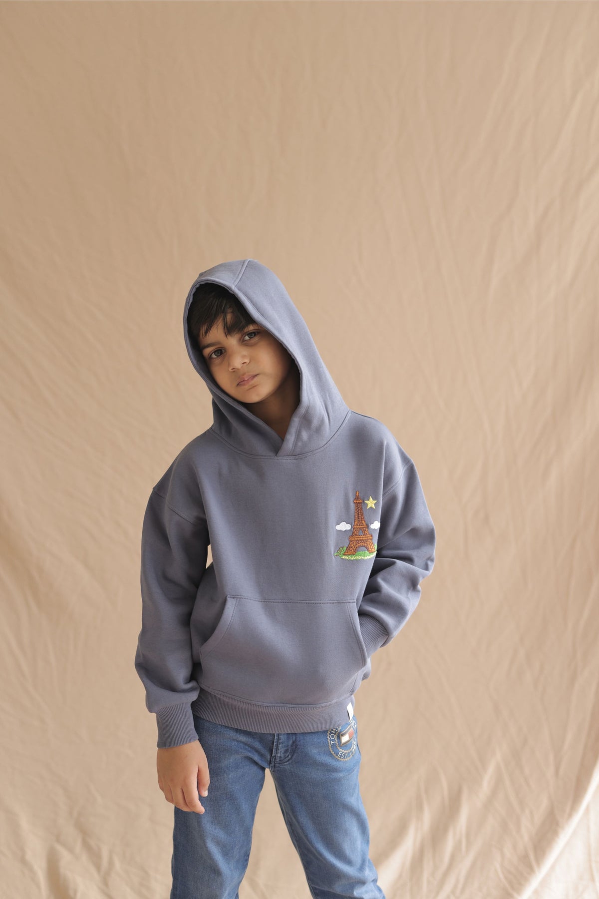 Denim blue kids hoodie with hood up and Eiffel tower embroidery, worn by child