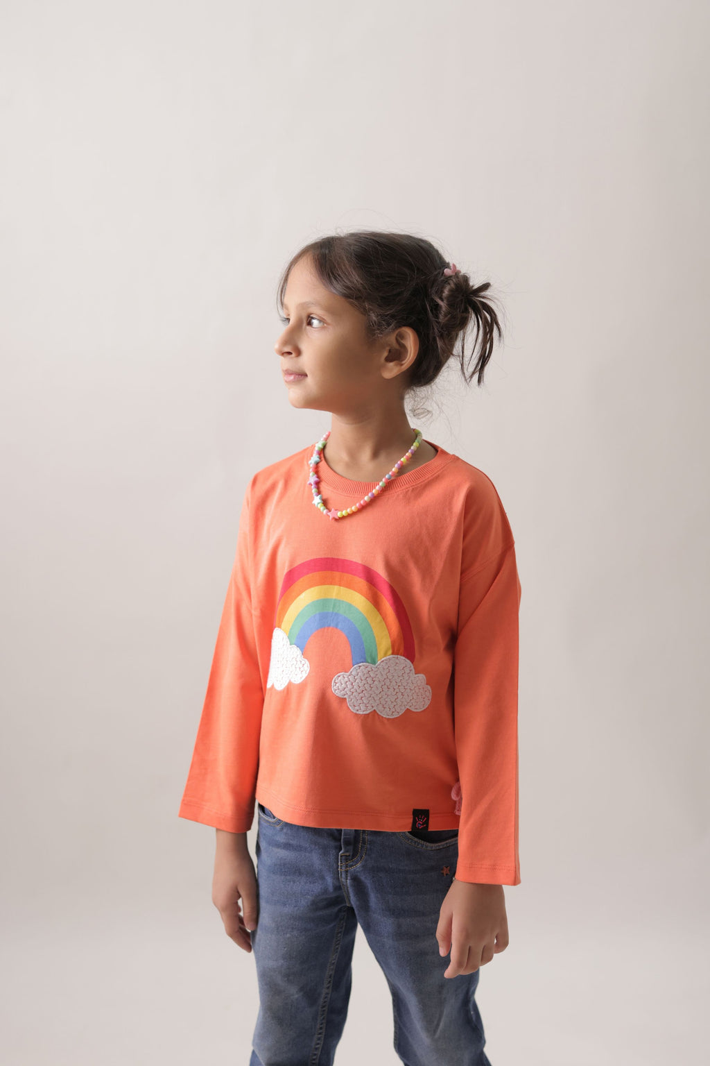 Girl wearing coral long-sleeve T-shirt with rainbow and embroidered clouds