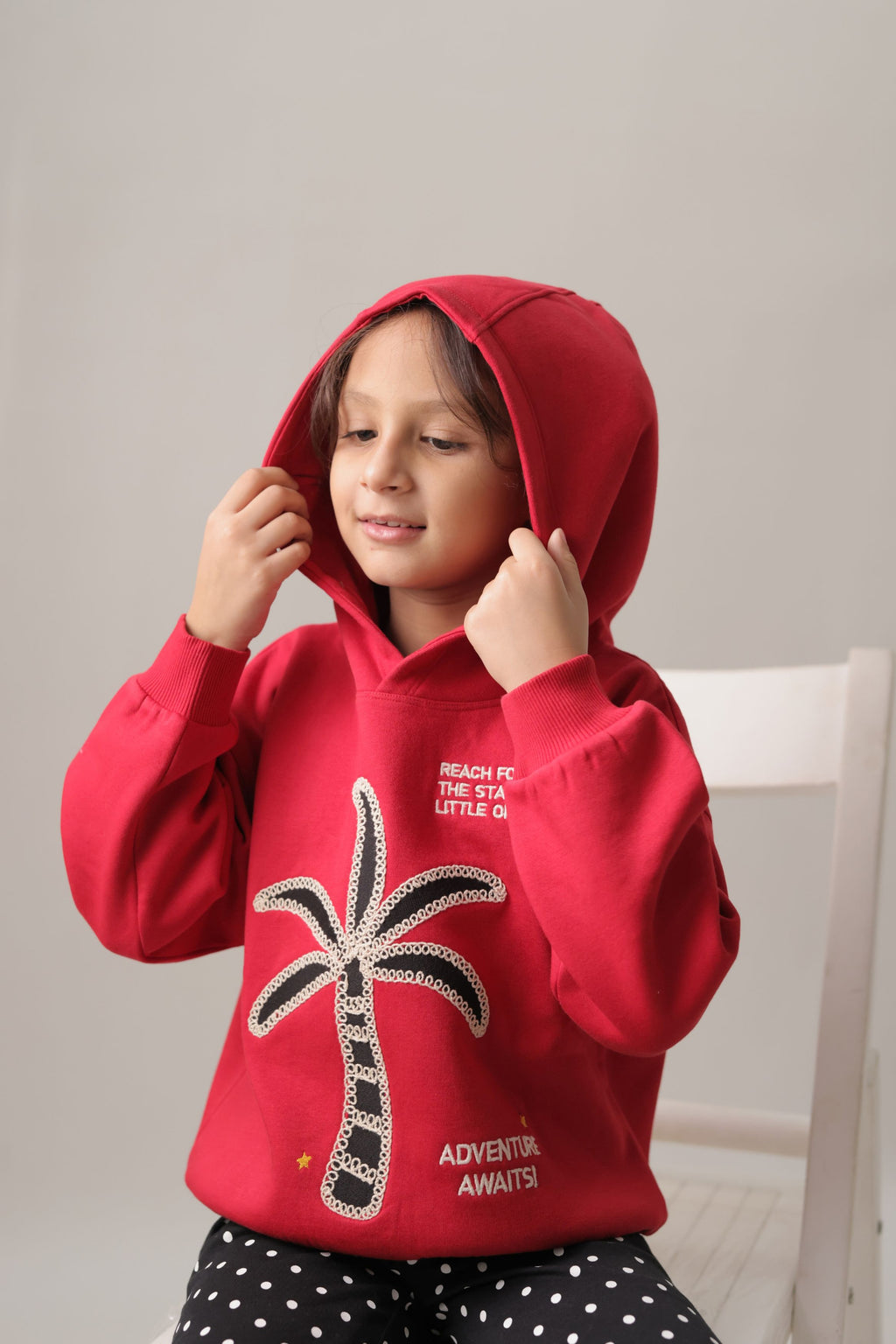 Red fleece hoodie on a child with hood up, palm tree embroidery on front