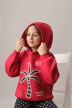 Red fleece hoodie on a child with hood up, palm tree embroidery on front