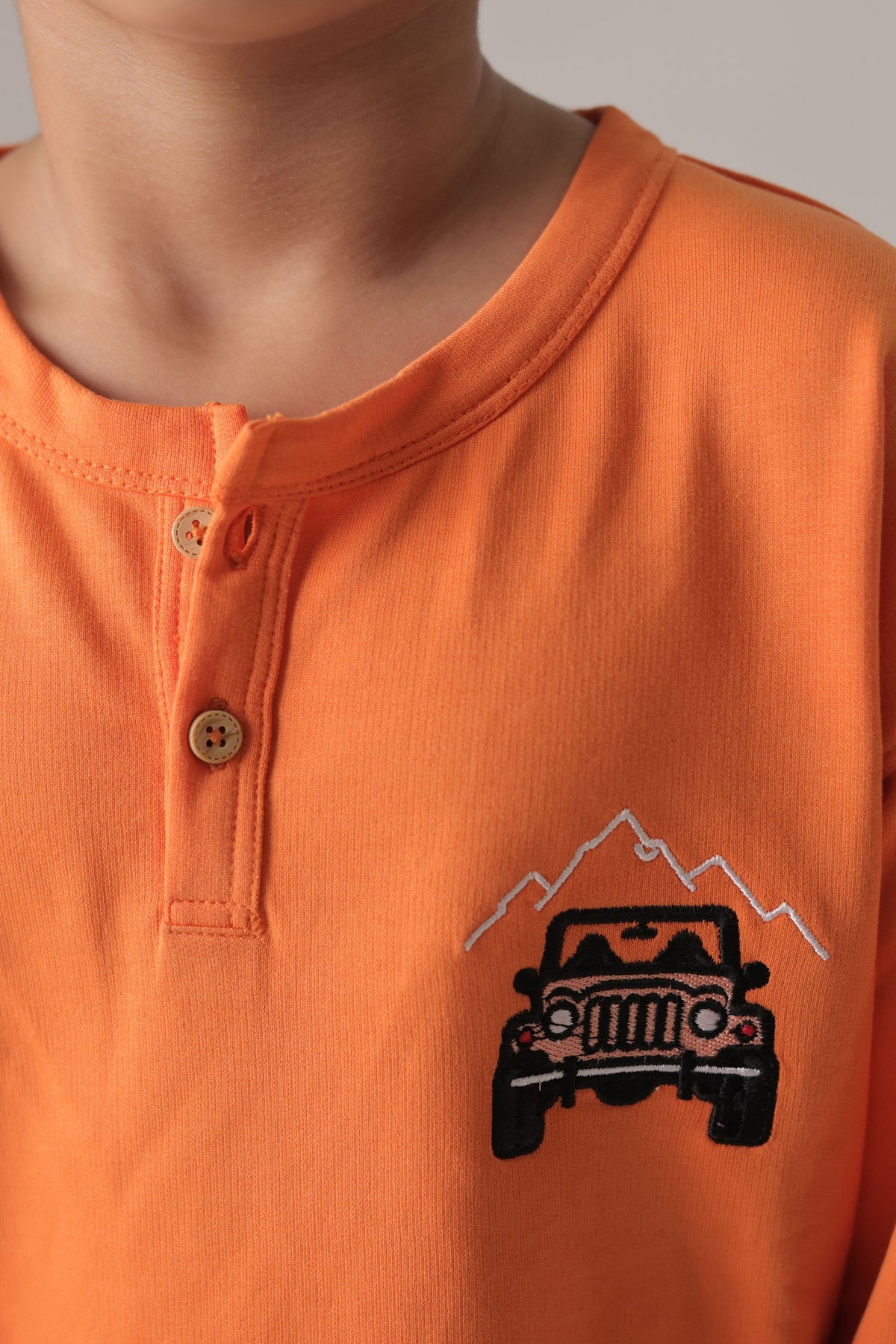 Orange boys henley T-shirt close-up: button placket and off-road car embroidery