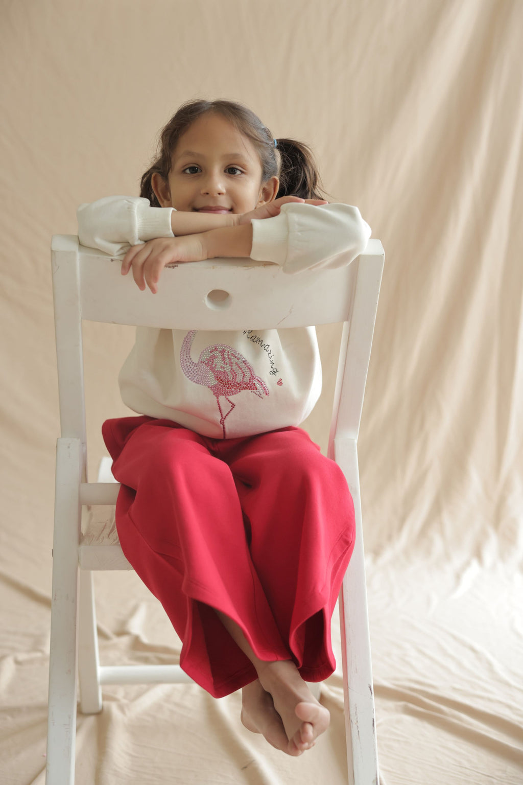 Girl in ivory cream hooded sweatshirt with flamingo embellishment while seated