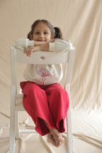 Girl in ivory cream hooded sweatshirt with flamingo embellishment while seated