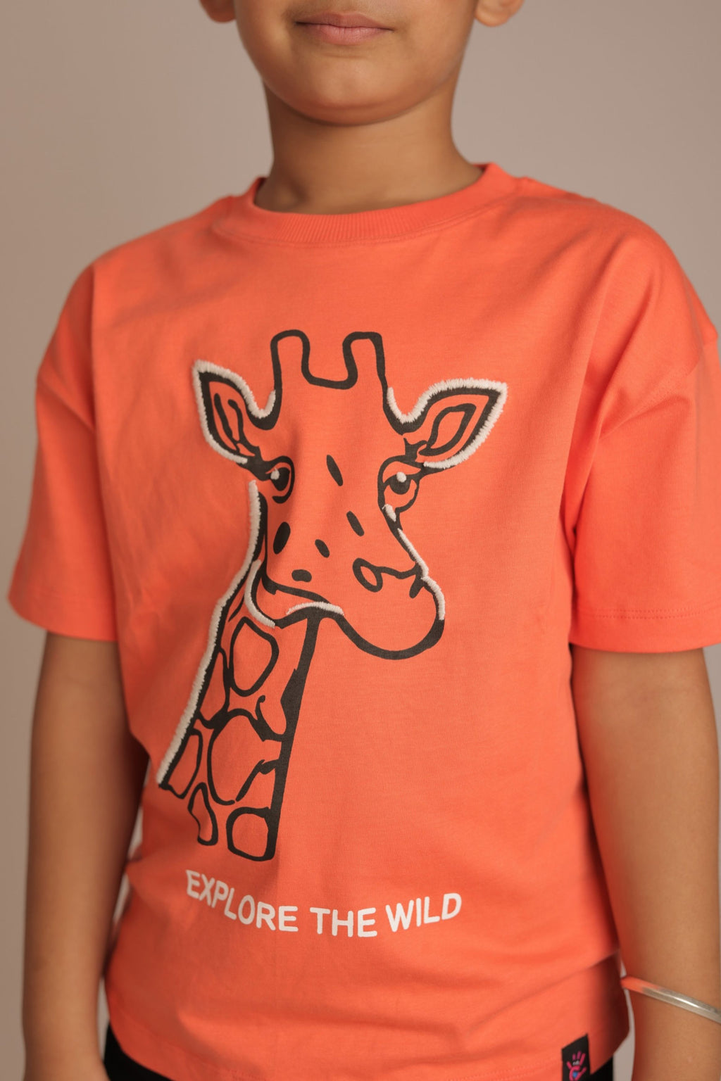 Orange comfort tee with embroidered giraffe outline and 'EXPLORE THE WILD' text (worn)