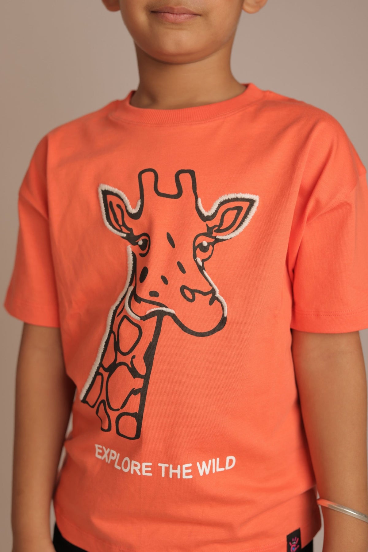 Orange comfort tee with embroidered giraffe outline and 'EXPLORE THE WILD' text (worn)