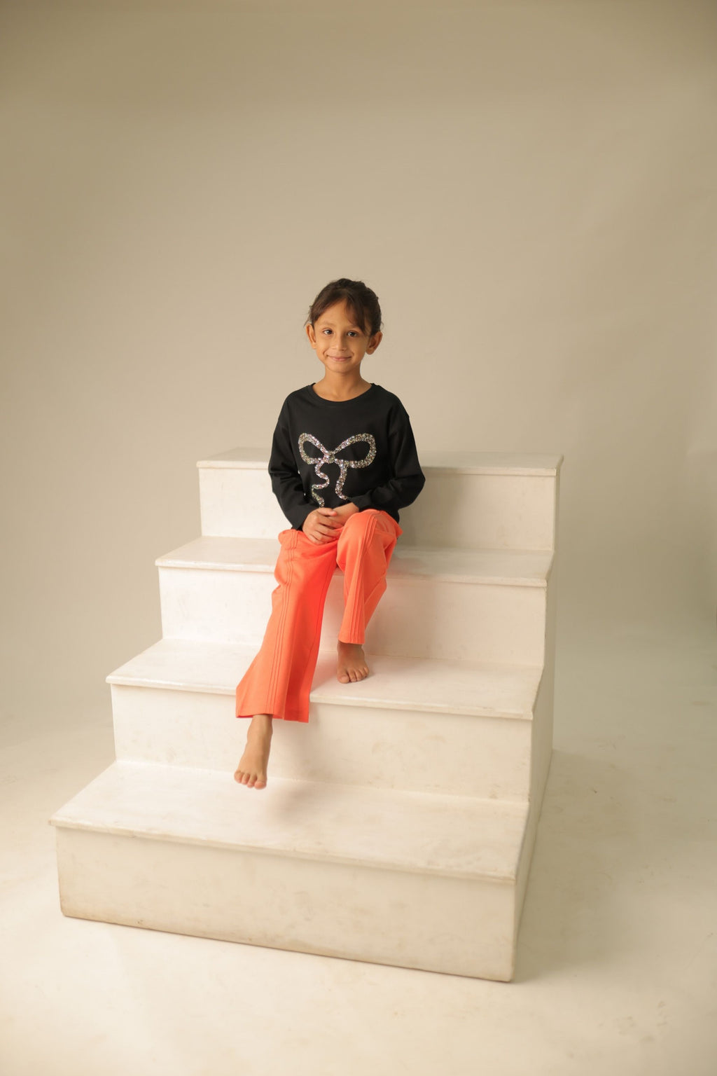 Child wearing black long-sleeve tee with gold-toned bead bow design