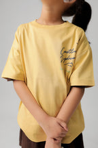 Kids sand yellow comfort tee with 'Chase the Coastal Breeze' script print on chest.
