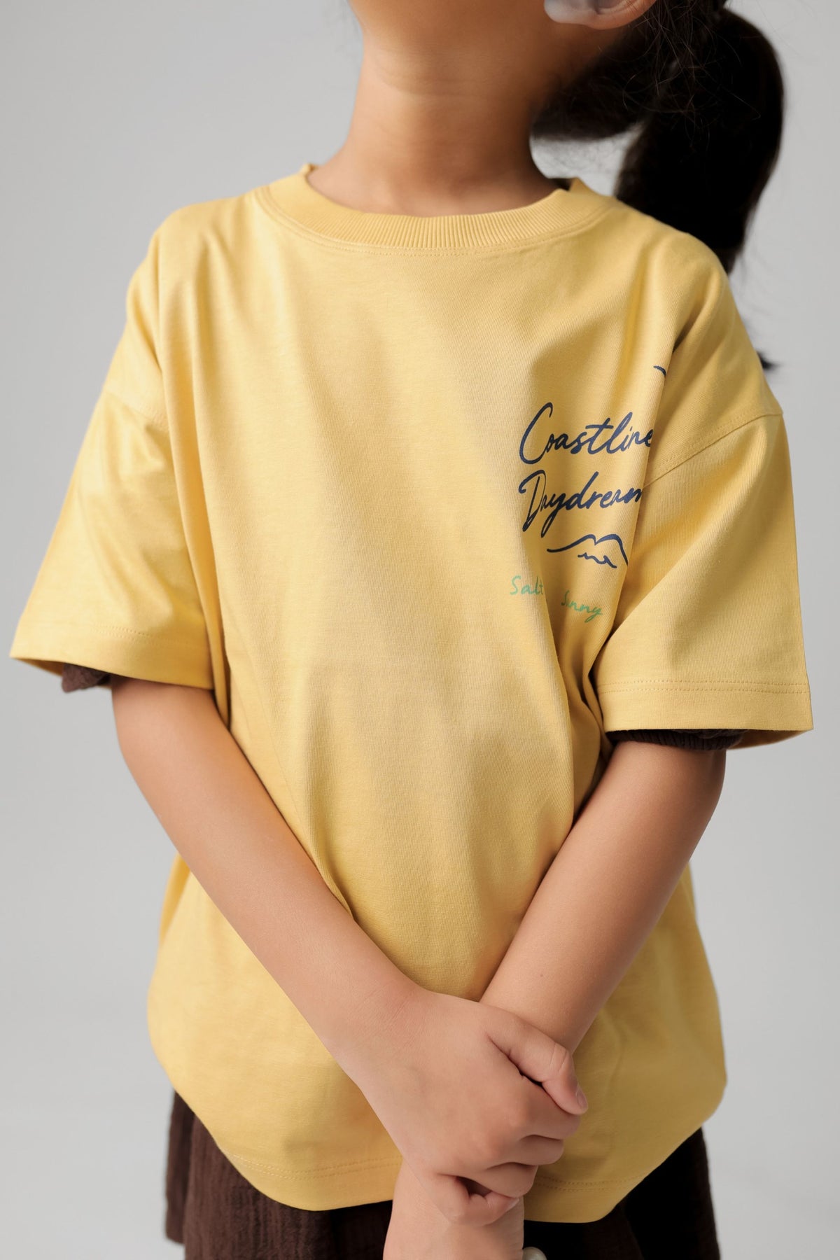 Kids sand yellow comfort tee with 'Chase the Coastal Breeze' script print on chest.