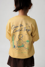 Kids sand yellow back graphic tee with surf boy, waves, and sun illustration.
