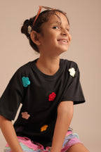 Black tee with colorful crochet flower appliques across the front, crew neckline