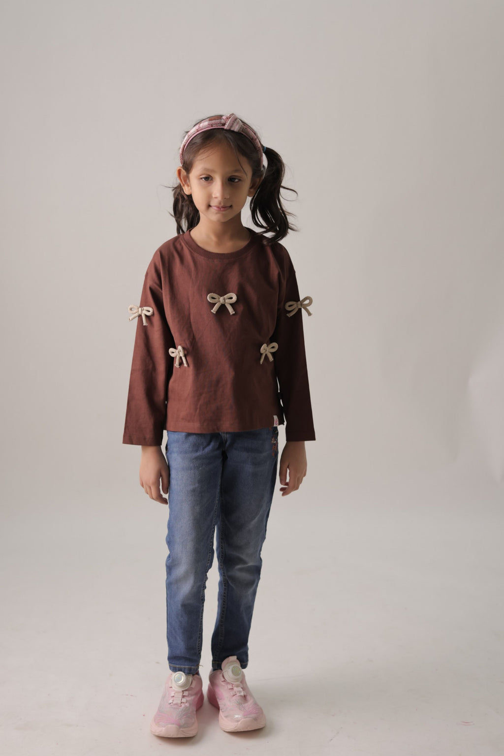 Dark brown long-sleeve tee with beige bow appliques, worn with blue jeans