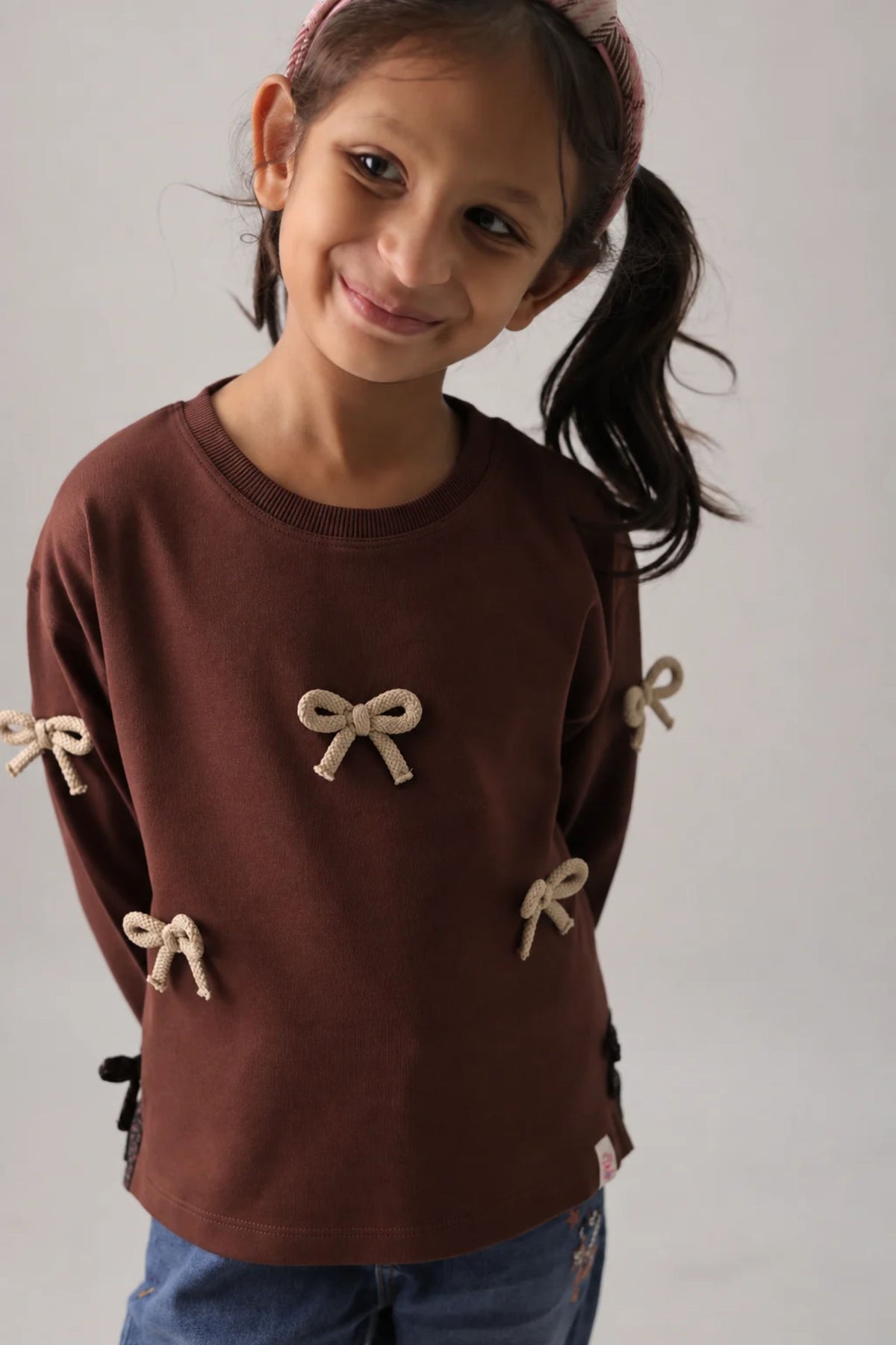 Dark brown long-sleeve kids' tee with beige bow appliques and side ribbon detail