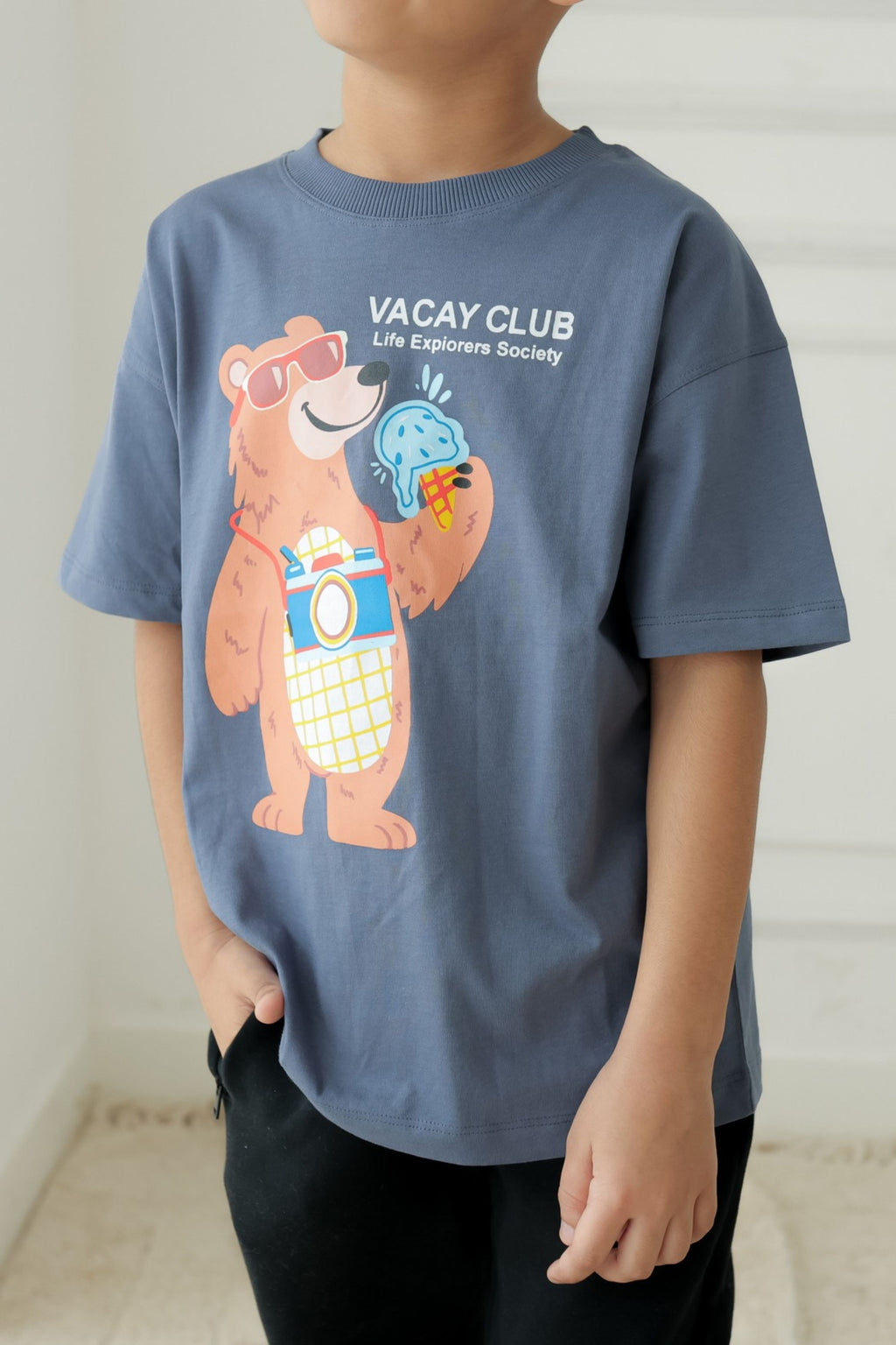 Kids round-neck comfort tee, blue, front view with “VACAY CLUB” bear graphic and slogan