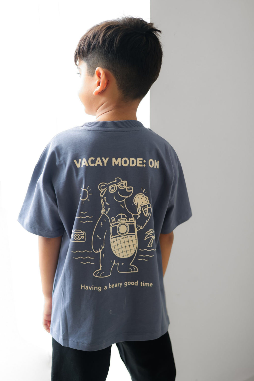 Kids round-neck comfort tee, blue, back view with “VACAY MODE: ON” bear line art and text