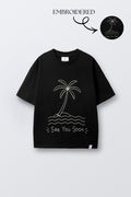 Black oversized t-shirt with embroidered palm tree, waves, and 'See You Soon' text