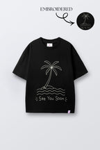 Black oversized t-shirt with embroidered palm tree, waves, and 'See You Soon' text