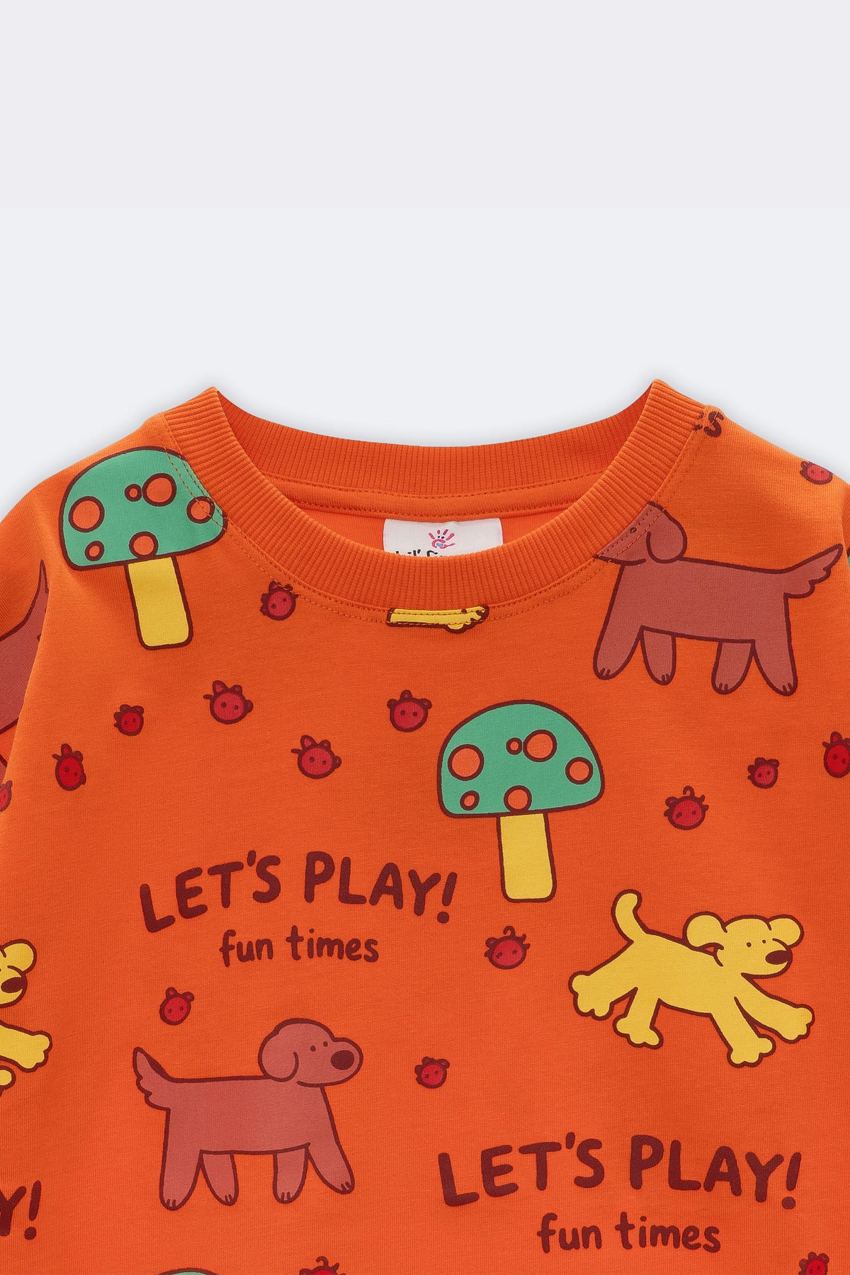 Orange kids tee close-up: “Let’s Play!” text with dogs, bugs, and mushroom icons