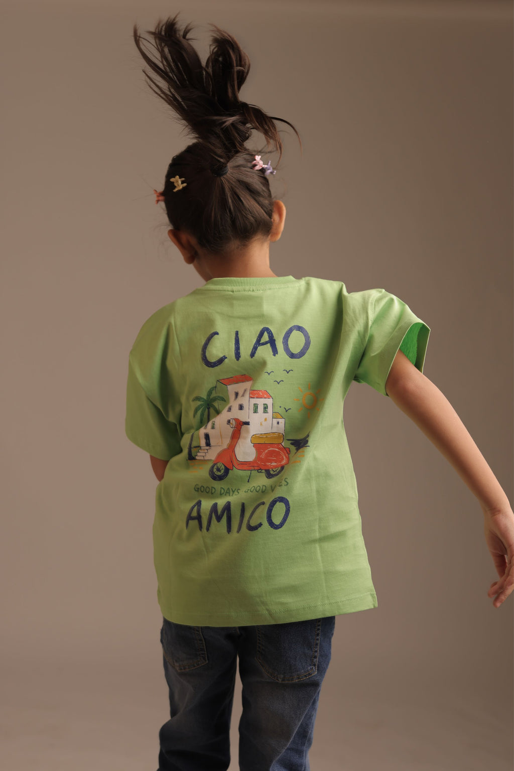 Back of kids green tee with “CIAO AMICO” text and scooter graphic, palm scene